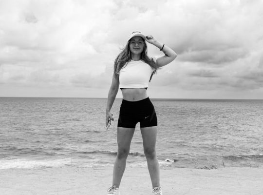 Black and white photo of a woman standing at the beach in Natal, Brazil, enjoying the ocean view.