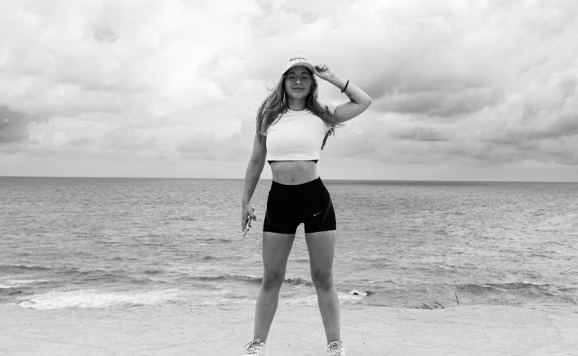 Black and white photo of a woman standing at the beach in Natal, Brazil, enjoying the ocean view.